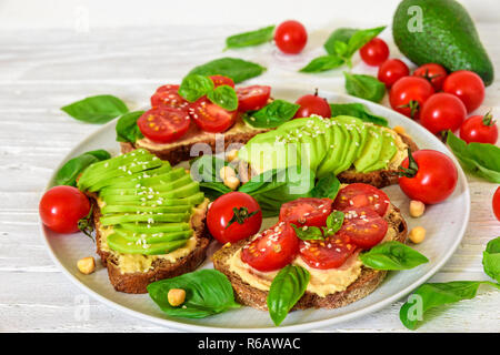 L'avocat et les tomates sandwiches avec du hoummos, sésame et basilic dans une plaque sur fond de bois blanc vegan aliments sains.. close up Banque D'Images