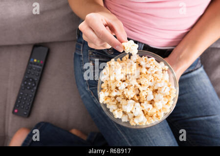 Woman Sitting on Sofa Eating Popcorn Banque D'Images