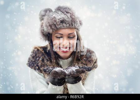 Belle jeune femme dans des vêtements d'hiver souffle les flocons de neige, qui tient dans ses mains. Banque D'Images