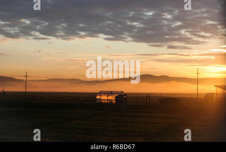 Lumière du soleil éclairant une serre dans une vallée de montagne brumeuse au lever du soleil, Transylvanie, Roumanie. Banque D'Images