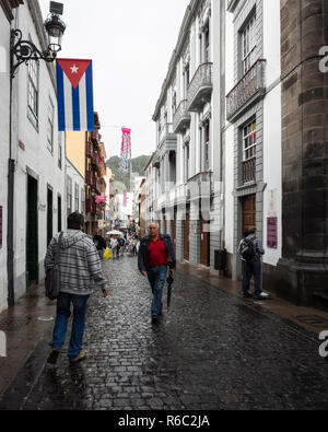 Santa Cruz. La Palma. L'Espagne. Les touristes et les habitants à marcher le long de la route pavée dans la partie ancienne de la ville. C'est juste cessé de pleuvoir et les surfaces de la route scintille à la lumière. Une montagne surplombe la rue dans le lointain. Banque D'Images