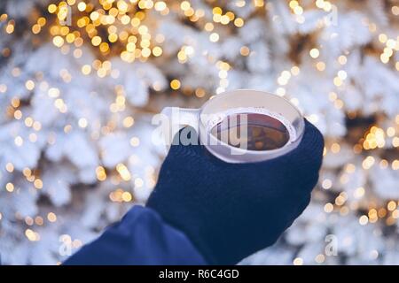 Man holding tasse de vin chaud contre l'arbre de Noël illuminé. Munich, Allemagne. Banque D'Images