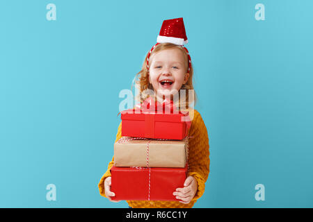 Heureux petite blonde enfant girl holding trois boîtes de cadeaux sur un fond isolé bleu. Le concept de célébrer, donner et recevoir un cadeau Banque D'Images