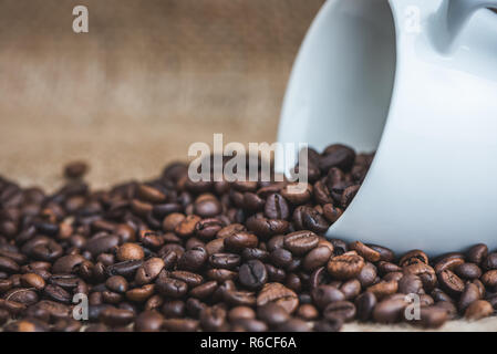 Les grains de café torréfié de renversé Tasse en céramique blanche sur fond de toile Banque D'Images