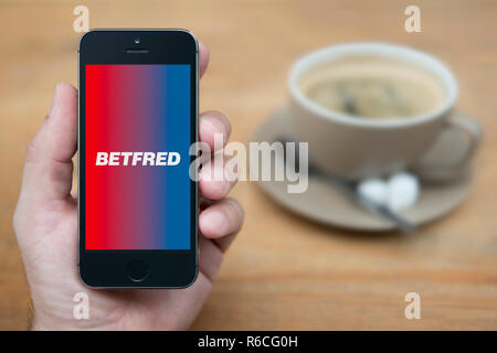 Un homme se penche sur son iPhone qui affiche le logo Betfred (usage éditorial uniquement). Banque D'Images