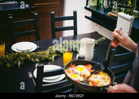 Femme met des plats faits maison. Les mains soigneusement appliquée à œuf frit plat de casserole. Le petit déjeuner pour deux personnes, à la cuisine à table à manger Banque D'Images