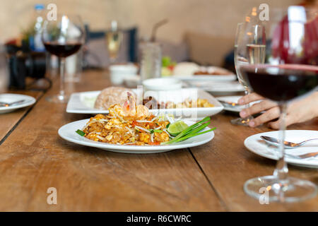 Célèbre nouilles pad thaï aux crevettes et un verre de vin rouge sur la table en bois. Banque D'Images