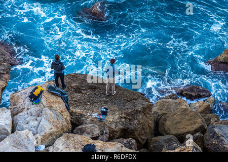 Nice, France - 2 octobre 2018 : les hommes à l'aide de crochet pour les poissons de pêche sur de gros rochers à la mer turquoise de la Méditerranée en matin de Nice, France. Banque D'Images