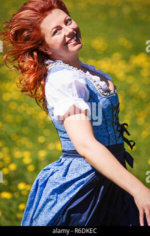 Belle Femme rousse avec un surpoids en Dirndl, exécutant de rire sur une prairie de fleurs. Banque D'Images