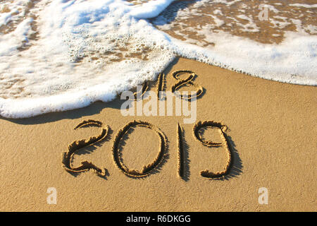 2019, 2018 ans écrit sur plage de sable de mer. Vague emporte en 2018. Banque D'Images