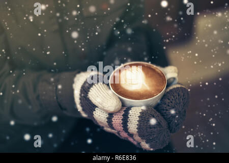 Femme de mains dans de chaudes mitaines en laine embrassant café chaud mug Banque D'Images
