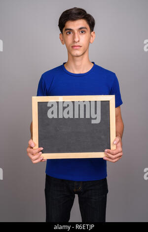 Young handsome Persian teenage boy holding empty blackboard with copy space Banque D'Images