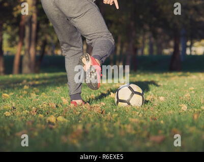 Soccer Player Kicking Football dans le parc dans le cadre d'une journée ensoleillée d'automne Banque D'Images