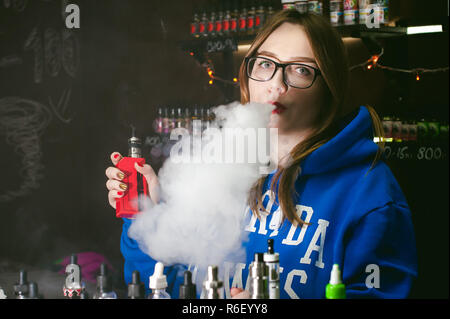 Jeune femme, le vendeur à vape shop shop, fumer la cigarette électronique, seine et libère un nuage de vapeur Banque D'Images