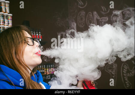 Jeune femme, le vendeur à vape shop shop, fumer la cigarette électronique, seine et libère un nuage de vapeur Banque D'Images