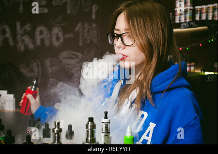 Jeune femme, le vendeur à vape shop shop, fumer la cigarette électronique, seine et libère un nuage de vapeur Banque D'Images