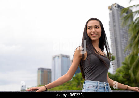 Happy young beautiful Asian woman smiling and thinking at the park Banque D'Images