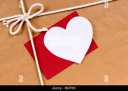 Cadeau Saint Valentin avec carte coeur blanc, enveloppe rouge, paquet de papier brun fond parcelle, copy space Banque D'Images