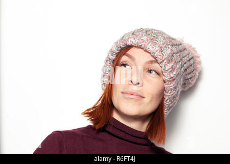 Portrait isolé de belle jeune fille rousse aux yeux verts à sideaways en violet et rose pull tricoté chapeau avec pompon habillé sideway Banque D'Images