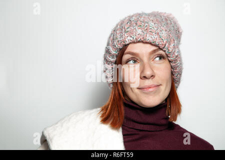 Portrait isolé de belle jeune fille rousse aux yeux verts et blancs chandail mauve et rose Chapeau tricoté avec pompon habillé latéralement smiling o Banque D'Images