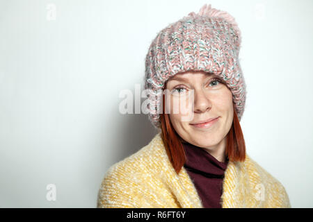 Portrait isolé de belle jeune fille rousse aux yeux vert jaune rose et mauve pull tricoté chapeau avec pompon habillé latéralement smiling sur w Banque D'Images