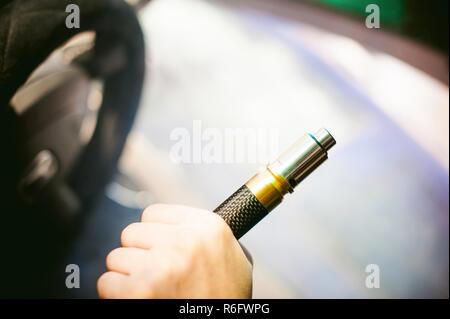 Jeune homme vaper avec barbe vaping mod mécanique. Guy fume une cigarette électronique en soufflant une vapeur de fumée. Tient dans la main sur fond coloré Banque D'Images