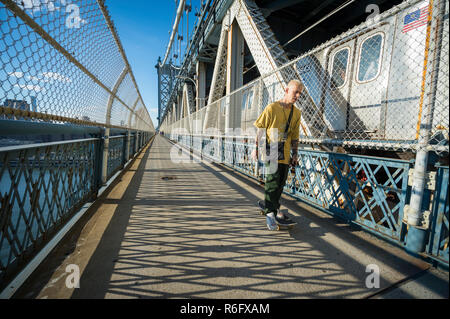 NEW YORK - AOÛT, 2017 : un jeune homme skateboards à côté d'un train de métro lié à Brooklyn, sur la promenade du pont de Manhattan. Banque D'Images