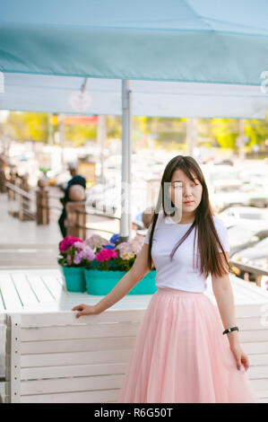 Cute asian young woman in cafe d'été à l'extérieur. fille en T-shirt blanc, avec de longs cheveux dans la lumière simple intérieur cosy restaurant de style urbain Banque D'Images