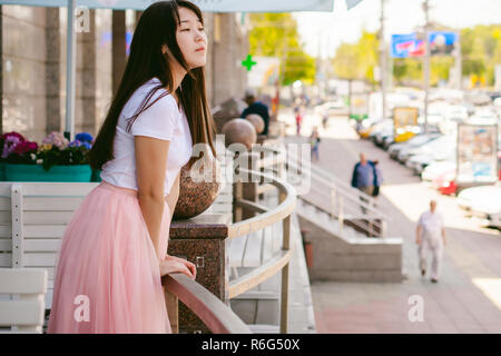 Cute asian young woman in cafe d'été à l'extérieur. fille en T-shirt blanc, avec de longs cheveux dans la lumière simple intérieur cosy restaurant de style urbain Banque D'Images