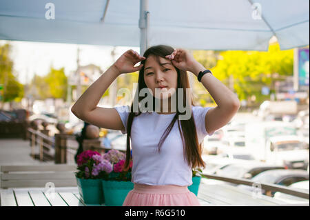 Cute asian young woman in cafe d'été à l'extérieur. fille en T-shirt blanc, avec de longs cheveux dans la lumière simple intérieur cosy restaurant de style urbain Banque D'Images