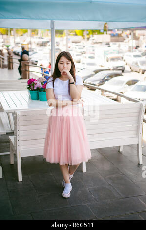 Cute asian young woman in cafe d'été à l'extérieur. fille en T-shirt blanc, avec de longs cheveux dans la lumière simple intérieur cosy restaurant de style urbain Banque D'Images