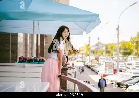 Cute asian young woman in cafe d'été à l'extérieur. fille en T-shirt blanc, avec de longs cheveux dans la lumière simple intérieur cosy restaurant de style urbain Banque D'Images