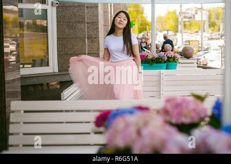 Cute asian young woman in cafe d'été à l'extérieur. fille en T-shirt blanc, avec de longs cheveux dans la lumière simple intérieur cosy restaurant de style urbain Banque D'Images