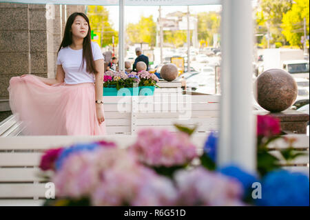 Cute asian young woman in cafe d'été à l'extérieur. fille en T-shirt blanc, avec de longs cheveux dans la lumière simple intérieur cosy restaurant de style urbain Banque D'Images