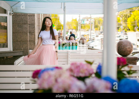 Cute asian young woman in cafe d'été à l'extérieur. fille en T-shirt blanc, avec de longs cheveux dans la lumière simple intérieur cosy restaurant de style urbain Banque D'Images