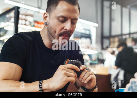 Close up of young man eating fresh burger juteux au café. Banque D'Images