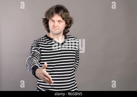 Un homme sérieux en noir et blanc à rayures pour homme offre sa main dans une poignée de main en signe de sincérité pour sceller une transaction commerciale, d'accueil ou en offrant ses félicitations sur fond gris. Banque D'Images