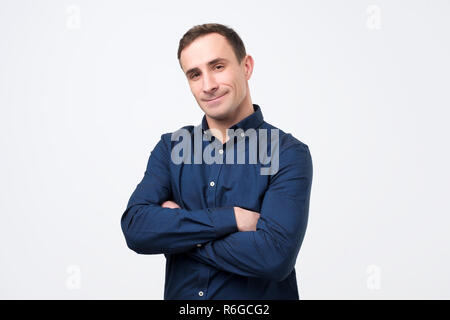 Smiling young man standing with arms crossed contre l'arrière-plan gris Banque D'Images