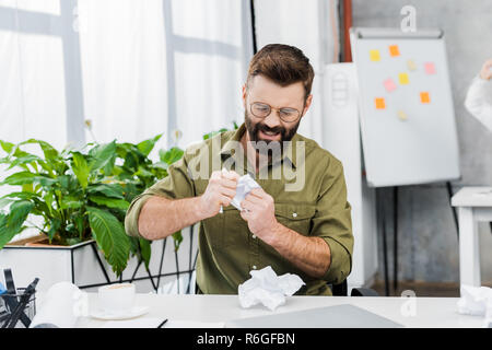 Angry businessman de déchirer le papier à table in office Banque D'Images
