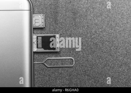 Téléphone mobile et d'emplacements ouverts pour nano cartes SIM, lecteur micro SD et clé de métal sur fond gris avec copie espace, photo en noir et blanc Banque D'Images