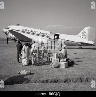 1959, historiques, les passagers debout à l'extérieur avec leurs bagages en attente d'un conseil royal à hélices de Nepal Airlines-Douglas DC3 avions stationnés sur une piste herbeuse à Katmandou (Népal). La compagnie aérienne la plus ancienne du pays, fondée en 1958, le DC-3 a son premier avion et utilisé pour servir des voies nationales et destinations en Inde. Banque D'Images