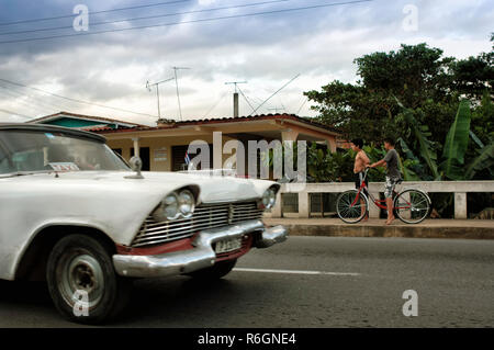Deux garçons à l'extérieur de leur maison, alors qu'une voiture blanche classique par les lecteurs. Pinar del Rio, Cuba Banque D'Images