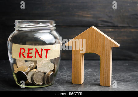 Bocal en verre avec des pièces de monnaie et l'inscription 'nt' et une petite maison en bois. Location de biens immobiliers, appartements. services d'un agent immobilier. le logement abordable, r Banque D'Images