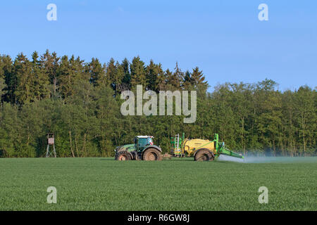 Agriculteur dans le tracteur l'épandage d'herbicides / insecticides / pesticides sur terrain avec pulvérisateur traîné au printemps Banque D'Images
