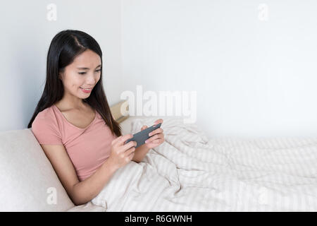 Femme jouant de jeu sur téléphone portable à l'intérieur de chambre à coucher Banque D'Images