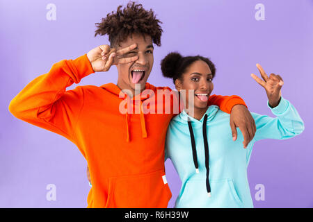 Photo de joyeux african american woman et montrant des signes de paix sur fond violet isolés Banque D'Images