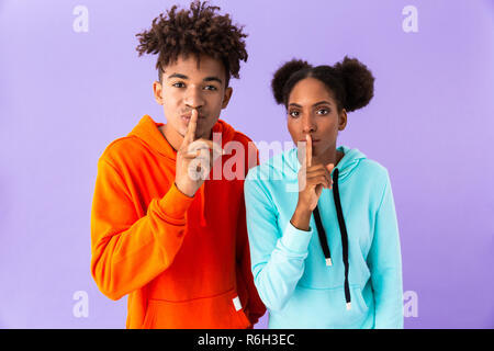 Photo de young african american guy and girl holding index sur lèvres sens isolé sur fond violet shh Banque D'Images