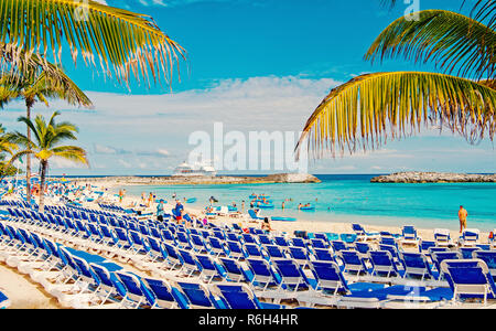 Great Stirrup Cay, Bahamas - 8 janvier 2016 : rangées de chaises longues bleu sur mer plage de sable blanc, de palmiers, de vert et de navire de croisière sur l'horizon. idyllique Vacances d'été et complexe. Paradise Banque D'Images