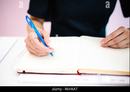 Femme d'affaires de prendre des notes dans le bloc-notes. Bien entretenu belle mains près des mains, en tenant un stylo, assis dans le lieu de travail Banque D'Images