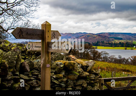 Panneau indiquant Pooley Bridge, Howtown et Auterstone sur le sentier Ullswater Way dans le Lake District anglais avec mur de pierre sèche en arrière-plan Banque D'Images